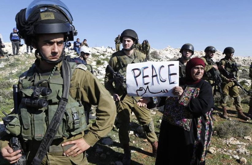 A protester holds a placard as she stands next to Israeli soldiers during a protest against Israeli settlements in Beit Fajjar town south of the West Bank city of Bethlehem (photo credit: REUTERS)