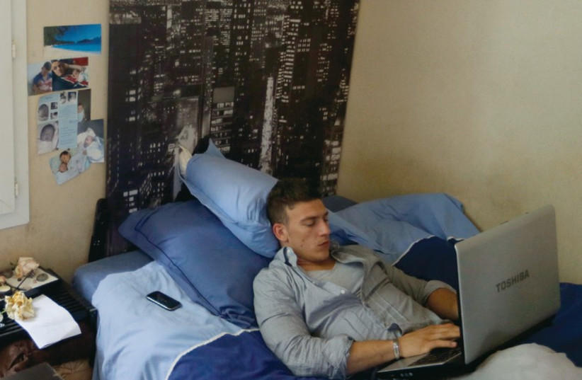A young man works from his laptop in his bedroom of his mother’s home in France. (photo credit: ILLUSTRATIVE: REUTERS)