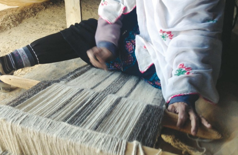 A woman hand-weaves a rug on a traditional loom. (photo credit: MEITAL SHARABI)