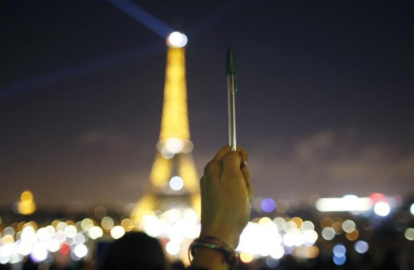 A person holds a pen, symbolizing freedom of speech, as lights on the Eiffel Tower start to dim before switching off for five minutes (photo credit: REUTERS)