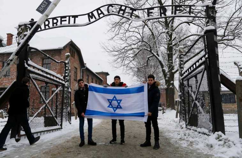 A group of visitors hold an Israeli flag in front of the gate of the former Nazi death camp of Auschwitz, January 26 (photo credit: REPRODUCTION)