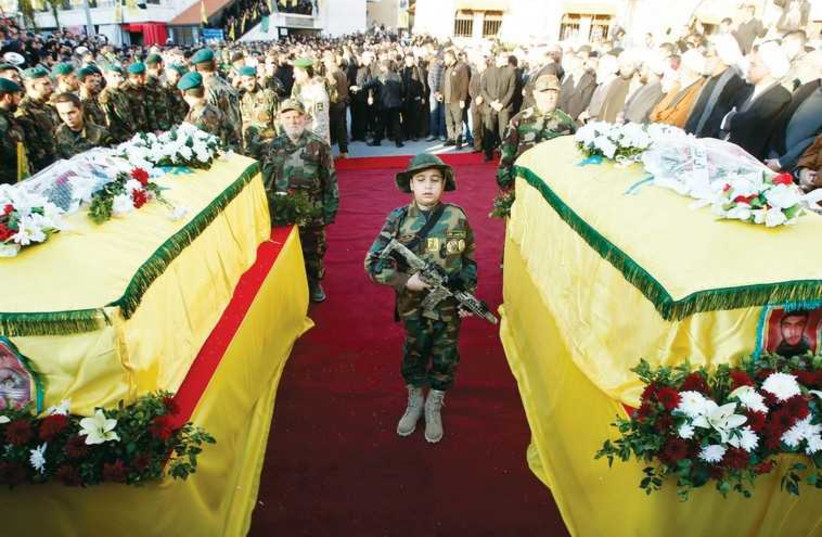 The son of Hezbollah soldier Abbas Hijazi, who died in an air strike in Quneitra, carries a toy weapon as he stands between the coffins of his father. (photo credit: REUTERS)
