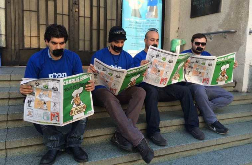 Yisrael Beytenu activists reading Charlie Hebdo with their mouths taped shut in front of Independence Hall in Tel Aviv (photo credit: Lahav Harkov)