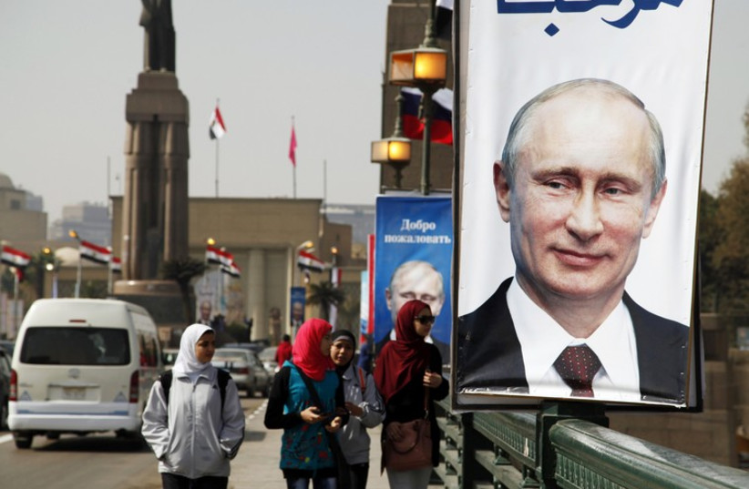 Girls walk past a banner with a picture of Russian President Vladimir Putin along a bridge, in central Cairo (photo credit: REUTERS)