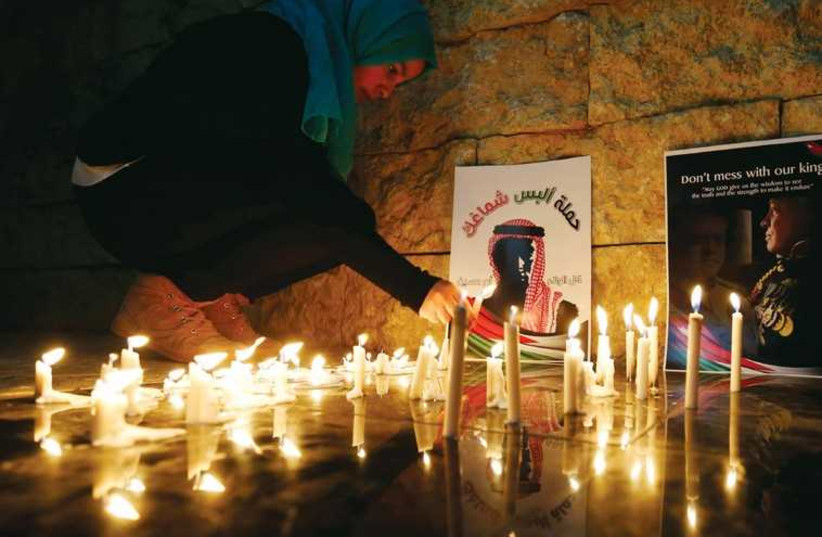 A woman lights a candle near a poster of Jordan’s King Abdullah II (photo credit: REUTERS)