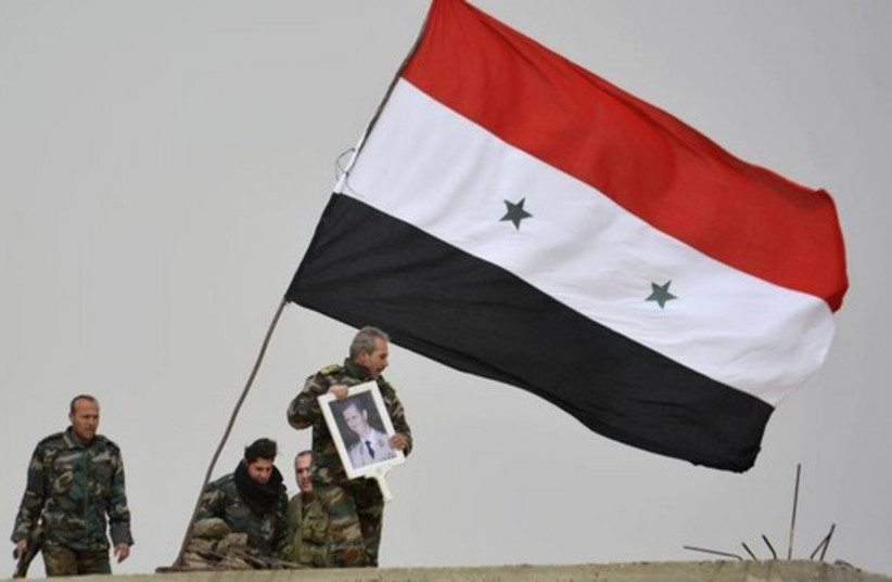 A fighter loyal to Syria's president Bashar Assad holds his picture as fellow fighters rest by a Syrian national flag after gaining control of the area in Deir al-Adas, a town south of Damascus (photo credit: REUTERS)