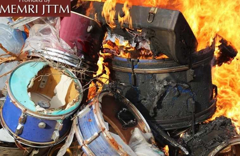 A group of masked ISIS members torching a pile of drums that were confiscated by the religious police. (photo credit: MEMRI)