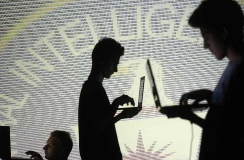 People are silhouetted as they pose with laptops in front of a screen projected with binary code and a Central Inteligence Agency (CIA) emblem (photo credit: REUTERS)
