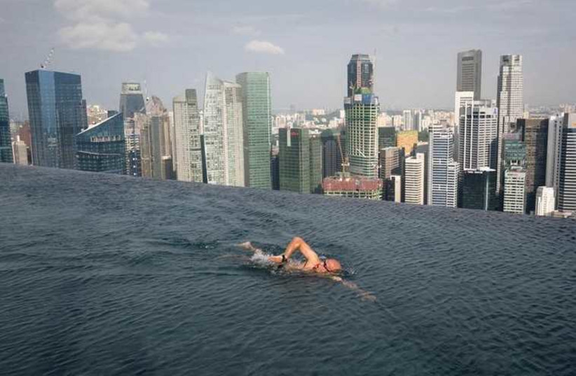 A guest swims in the infinity pool of the Skypark that tops the Marina Bay Sands hotel towers in Singapore (photo credit: REUTERS)