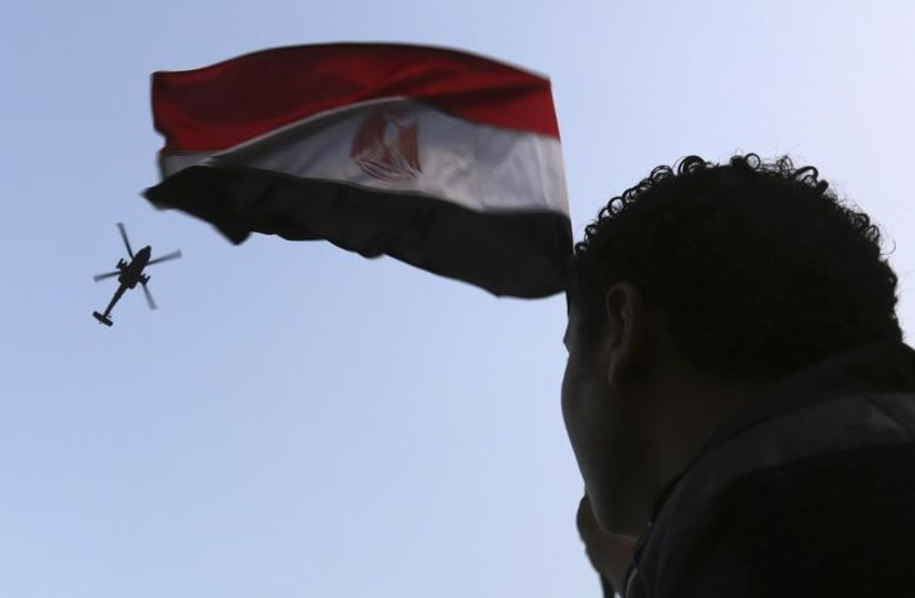 An Egyptian military helicopter, trailing a national flag, circles over Tahrir Square (photo credit: REUTERS)