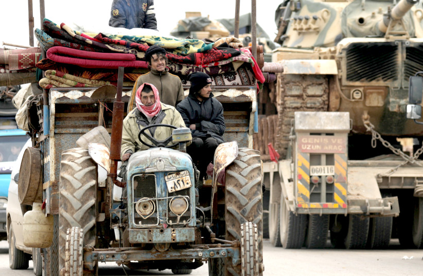 INTERNALLY DISPLACED Syrians from the western Aleppo countryside ride on a tractor with their belongings past Turkish military vehicles, in Hazano near Idlib on February 11. (photo credit: KHALIL ASHAWI / REUTERS)
