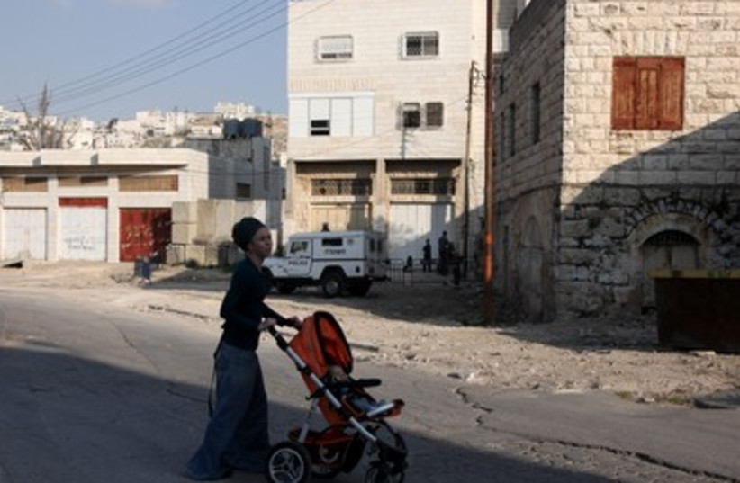 A Jewish woman wheels her child by the Hebron home