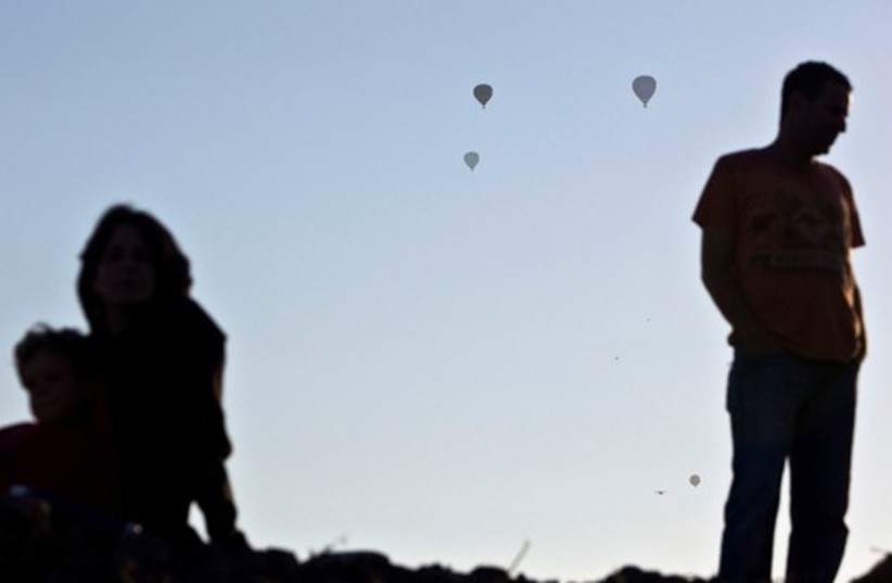 People are silhouetted as they watch hot air balloons fly 