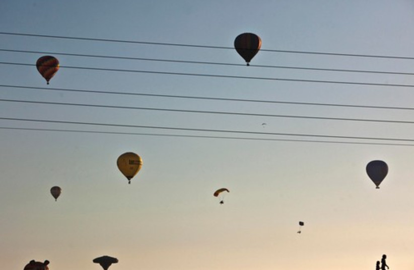Children are silhouetted as hot air balloons and paragliders