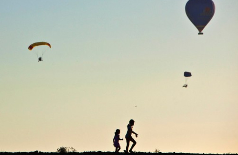 Children are silhouetted as a hot air balloon (R) and paragl