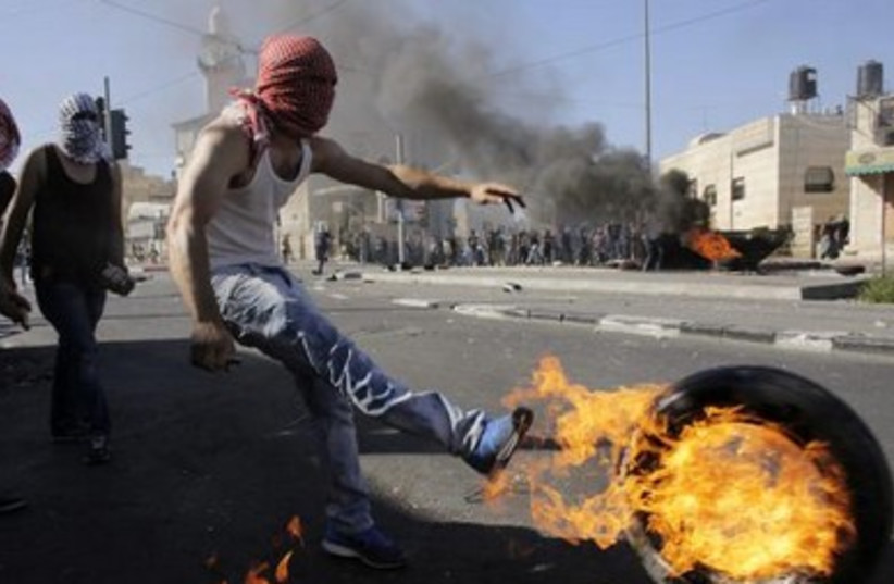 A Palestinian kicks a burning tire during riots in the east Jerusalem neighborhood of Shuafat.