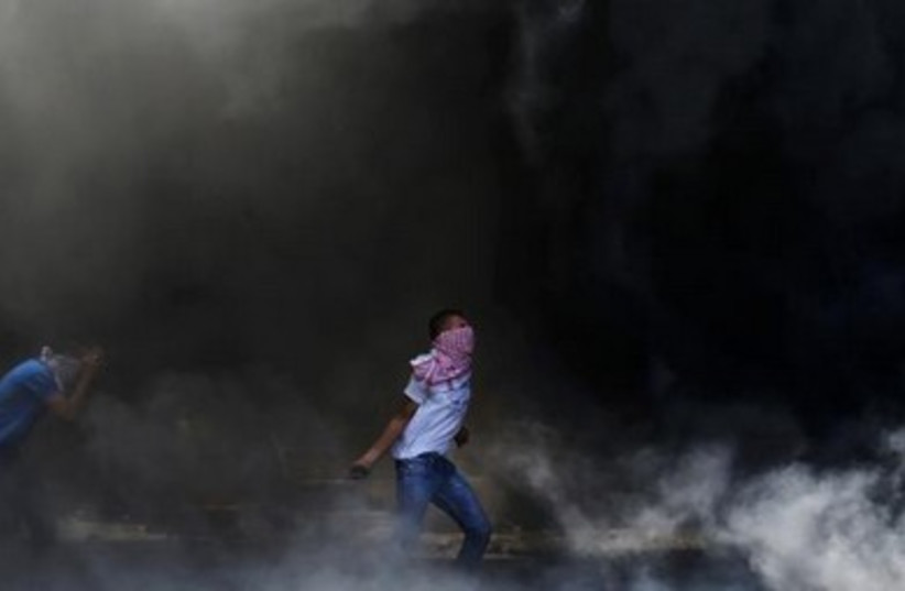 A Palestinian prepares to hurl a stone as he stands in a cloud of smoke from tires set ablaze during clashes with Israeli police in Shuafat. 