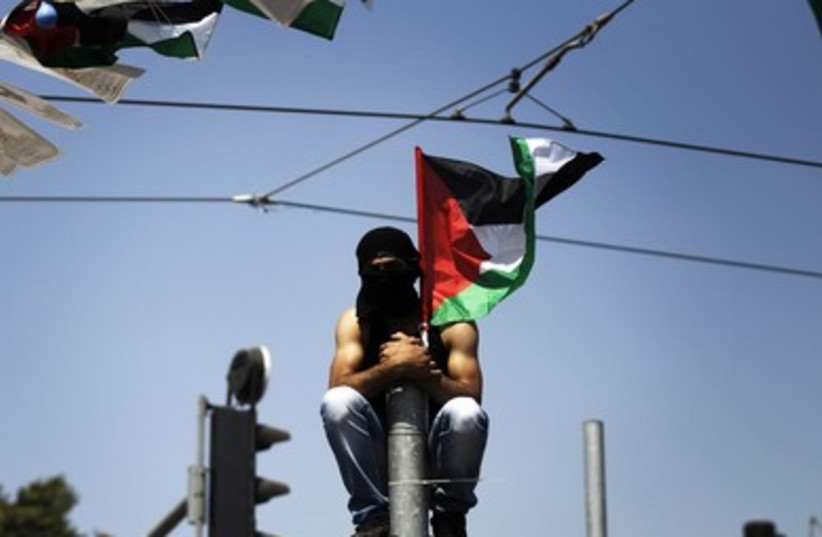 A masked Palestinian youth looks on from atop a pole during the funeral of 16-year-old Muhammad Abu Khdeir in Shuafat.