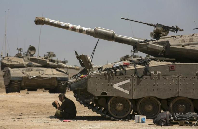 An Israeli soldier sits next to tanks at a staging area near the border with the Gaza Strip