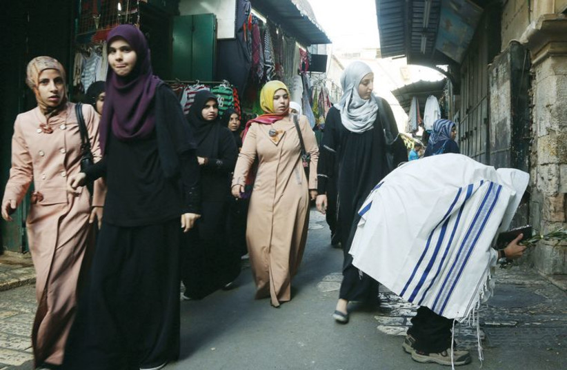 A man prays during Hoshana Raba as Palestinian women walk past.