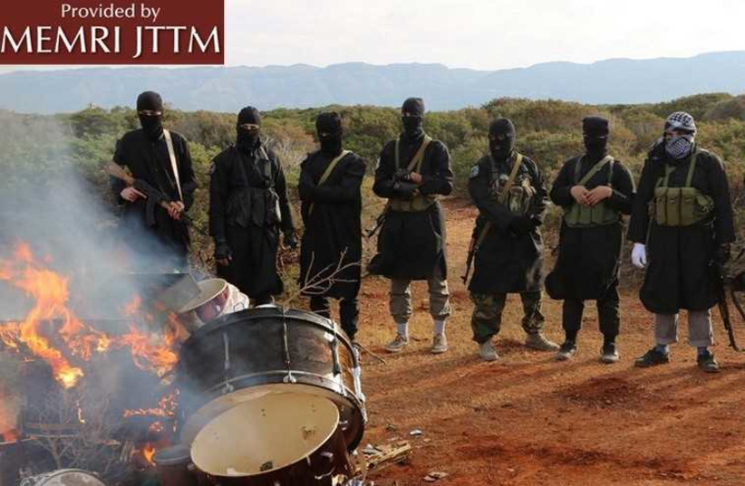 A group of masked ISIS members torching a pile of drums that were confiscated by the religious police.