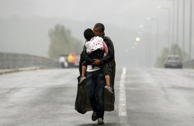 A Syrian refugee kisses his daughter as he walks through a rainstorm towards Greece's border with Macedonia, near the Greek village of Idomeni