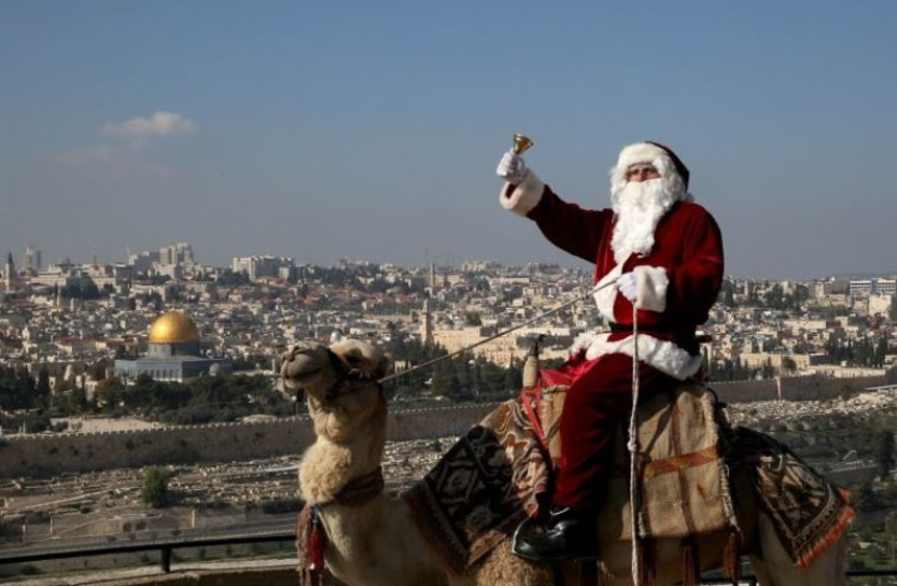A Christian man dressed up as Santa Claus rings a bell as he sits on a camel at Mt. Olives back-dropped by Jerusalem's Old City skyline