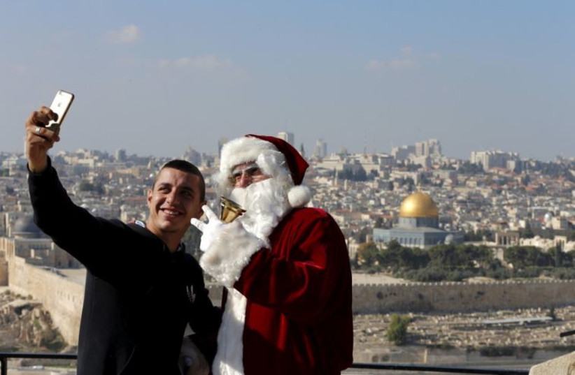 A man takes a selfie with Israeli-Arab Issa Kassissieh as he wears a Santa Claus costume during an annual Christmas tree distribution by the Jerusalem municipality on the Mount of Olives