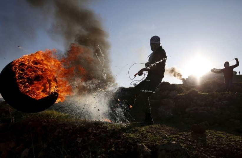 A Palestinian protester kicks a burning tire during clashes with Israeli troops near Ramallah