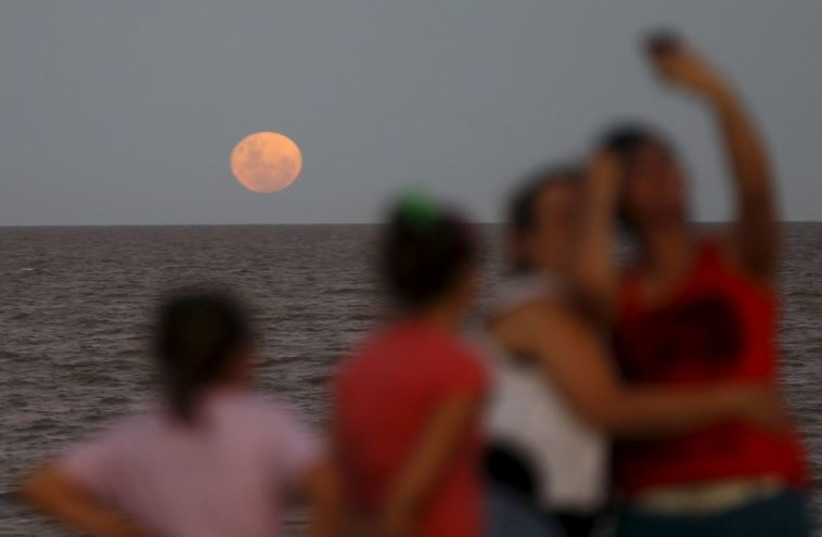 People take a selfie as a full moon rises over the Buenos Aires sky