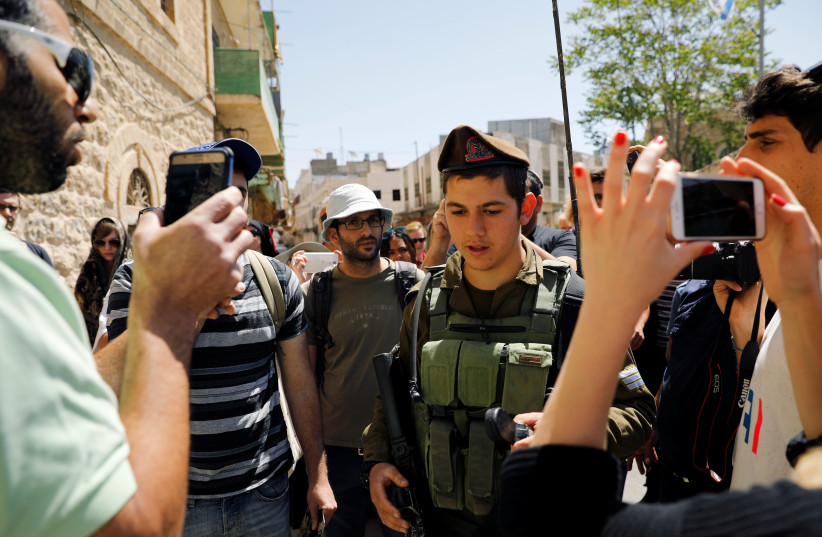 An Israeli soldier stands between an Israeli settler (L) and visitors on a tour held by leftwing NGO "Breaking the Silence" in the West Bank city of Hebron April 19, 2017. Picture taken April 19, 2017. (photo credit: REUTERS)