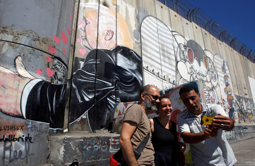 Tourists stand in front of a grafitti depicting US President Donald Trump on the controversial Israeli barrier in the West Bank town of Bethlehem August 4, 2017.  (photo credit: REUTERS)