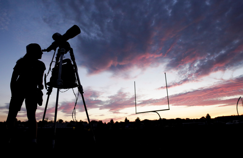 A woman looks through a telescope  the evening before a solar eclipse in Madras, Oregon, U.S. (credit: JASON REDMOND/REUTERS)