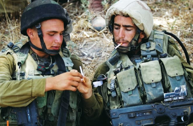 IDF soldiers share cigarettes while resting in the shade near the central Gaza Strip in July 2014. (photo credit: FINBARR O'REILLY / REUTERS)