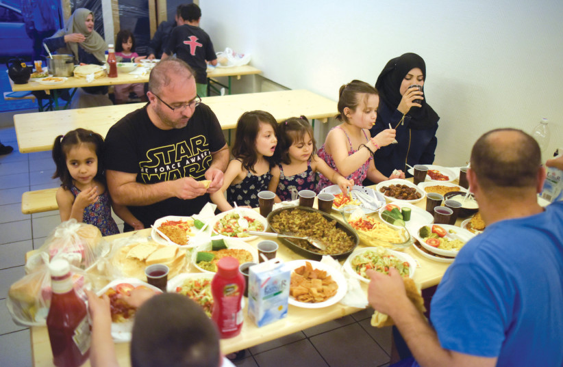 MEMBERS OF a Syrian family eat at a refugee shelter in a former hotel in Berlin in 2016 (photo credit: STEFFI LOOS /REUTERS)