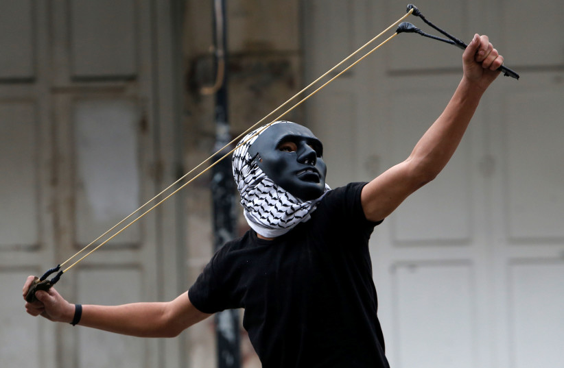 A Palestinian demonstrator uses a slingshot to hurl stones towards Israeli troops during clashes at a protest as Palestinians call for a 'Day of Rage.' (photo credit: REUTERS)
