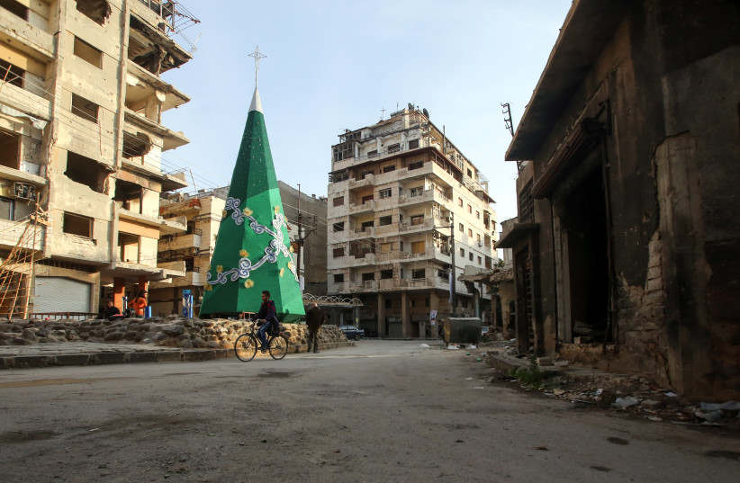 A Syrian man cycles past a Christmas tree being decorated in the Christian-majority neighbourhood of Hamidiyeh in the old city of Homs (photo credit: YOUSSEF KARWASHAN / AFP)