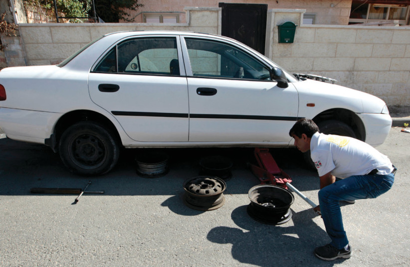 A man changes the tire on a car in Abu Ghosh, near Jerusalem (photo credit: AMMAR AWAD/REUTERS)
