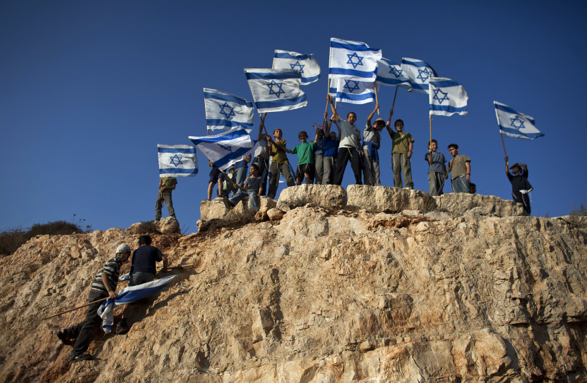 Jewish youth hold Israeli flags at the beginning of a rally march in the West Bank settlement of Itamar, near Nablus. (photo credit: NIR ELIAS / REUTERS)