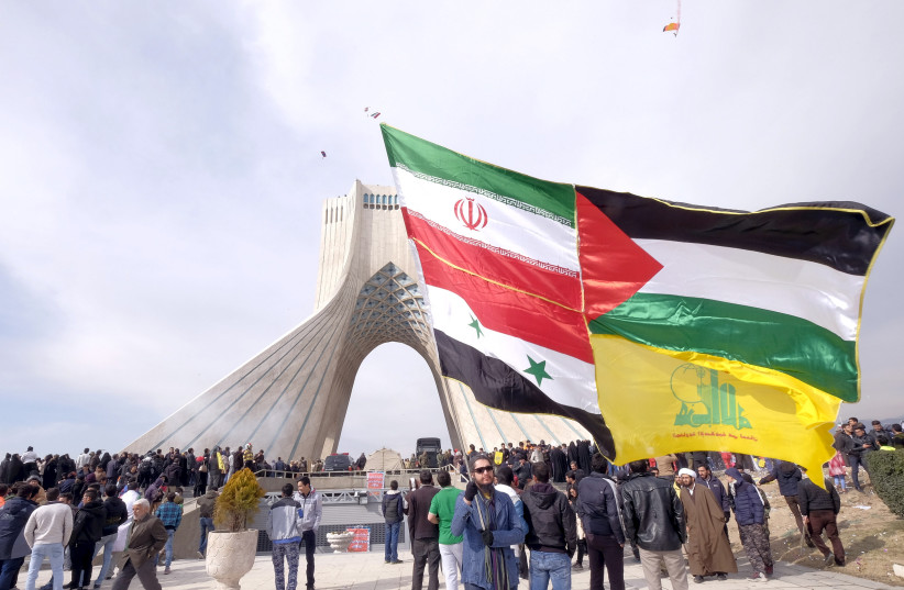 A man carries a giant flag made of flags of Iran, Palestine, Syria and Hezbollah, during a ceremony marking the 37th anniversary of the Islamic Revolution, in Tehran, Feburary 2016 (photo credit: RAHEB HOMAVANDI/REUTERS)