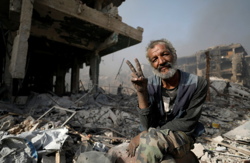 A man gestures as he sits on the rubble of damaged buildings in al-Hajar al-Aswad, Syria May 21, 2018. (photo credit: OMAR SANADIKI/REUTERS)