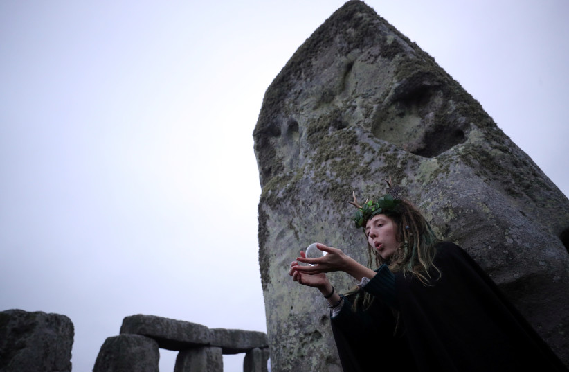 A reveller holds a crystal ball as the sun rises during the winter solstice at Stonehenge on Salisbury Plain in southern England, Britain, December 22, 2017. (credit: HANNAH MCKAY/ REUTERS)