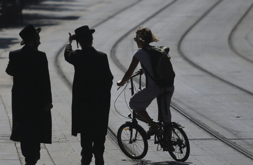 A secular woman cycles in downtown Jerusalem, alongside ultra-Orthodox pedestrians (photo credit: MARC ISRAEL SELLEM)