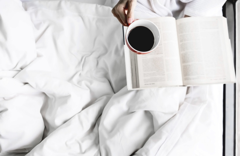 Photo of woman on the bed with old book and cup of coffee (photo credit: INGIMAGE)