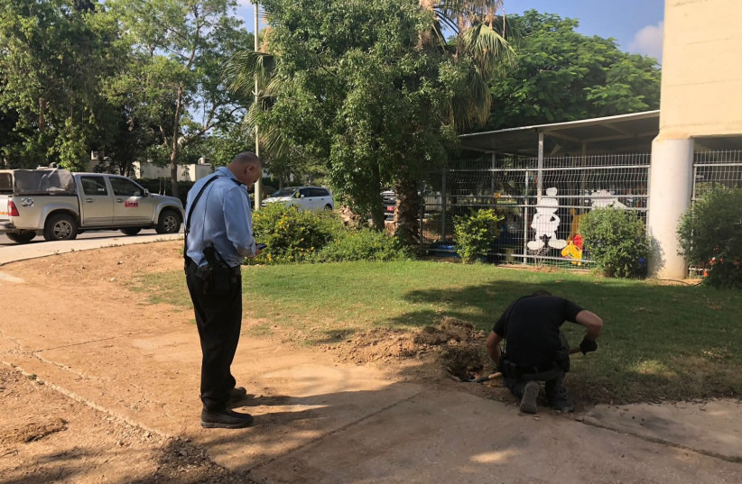 A worker digs up fragments from a projectile fired from Gaza that landed next to a kindergarten, June 20th 2018 (photo credit: ESHKOL REGIONAL COUNCIL)