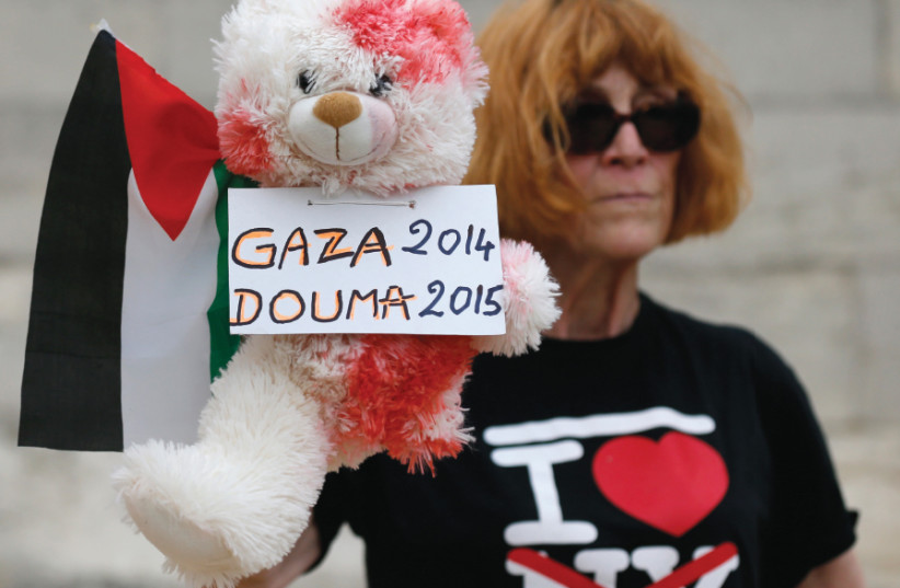  A WOMAN holds a stuffed bear, covered in fake blood, and a Palestinian flag to protest the ‘Tel Aviv on Seine’ event on an artificial sand beach in Paris on August 13, 2015. Leftist critics branded the event ‘indecent’ following an arson attack on a Palestinian family’s home in the West Bank villag (photo credit: REUTERS)