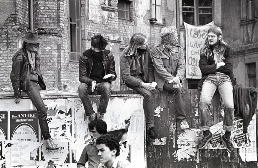 YOUNG ADULTS sit on a fence in Berlin in 1986 (photo credit: Wikimedia Commons)