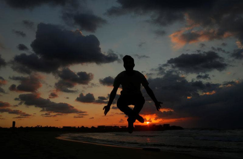 A Palestinian man jumps during the last sunset in 2016 at a beach in the northern Gaza Strip December 31, 2016. (photo credit: REUTERS/SUHAIB SALEM)