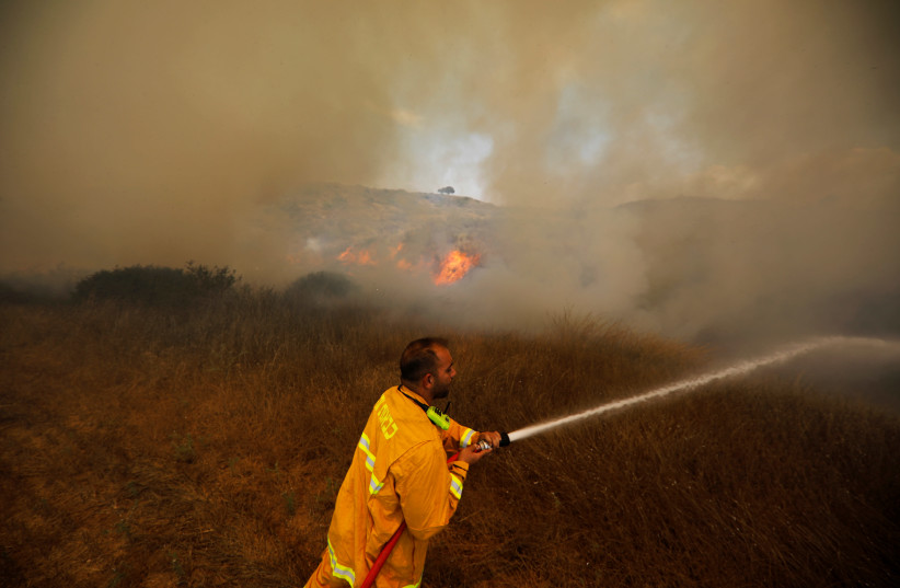 A firefighter attempts to extinguish a fire burning scrubland in an area where Palestinians have been causing blazes by flying kites and balloons loaded with flammable materials, on the Israeli side of the border between Israel and the Gaza Strip, near kibbutz Nir Am, June 5, 2018 (photo credit: AMIR COHEN/REUTERS)