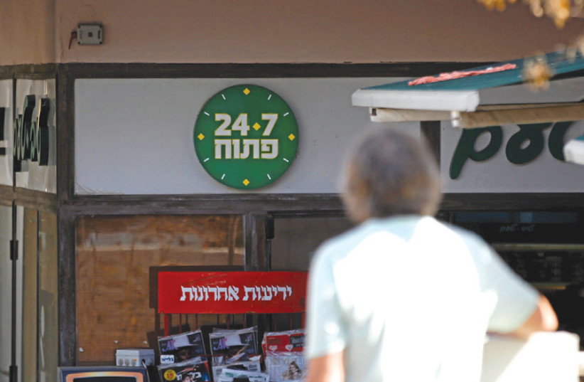 A man stands outside a Tel Aviv supermarket open 24/7, including Shabbat (photo credit: BAZ RATNER/REUTERS)